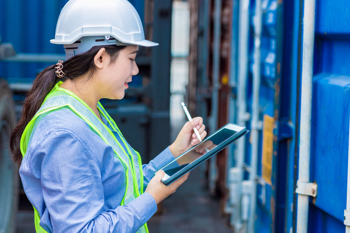 A customs broker in a white hard hat taking notes on a tablet in El Paso.